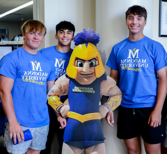 three students stand smiling with a cutout of Cruzer