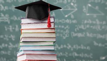 a stack of books in front of a chalk board with a graduation cap on top