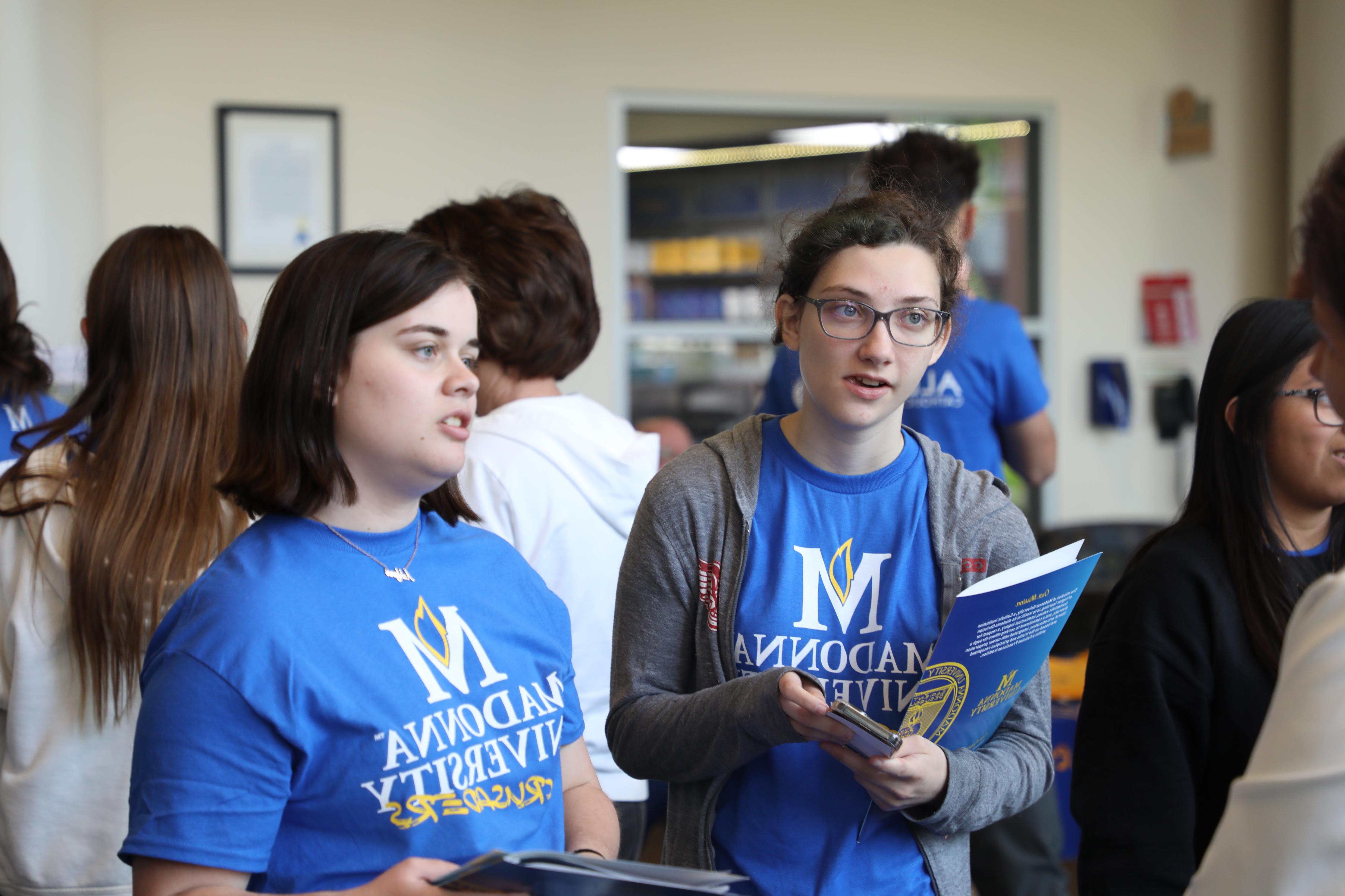 two students in Madonna University shirts listening to someone behind the camera