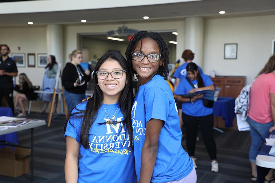 Two girls smile for the camera wearing madonna university shirts at orientation