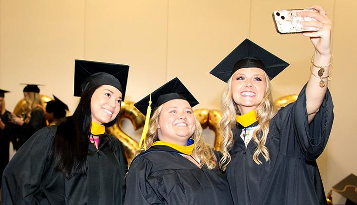 3 girls at graduation taking a selfie in academic regalia