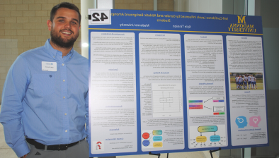 Kyle Tinnion smiling next to his research board at the 2023 Research Symposium