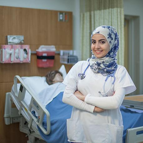 nursing student smiles while crossing arms standing in front of hospital bed in sim lab